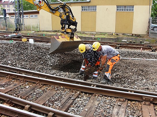 Zwei Arbeiter räumen ein altes Weichenteil aus dem Weg.