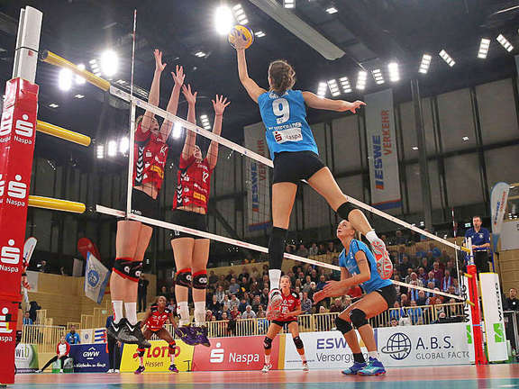 Three women jump up the volleyball net to attack