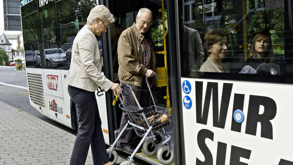 Senioren mit Rollator steigen in einen Bus.
