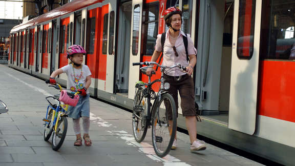 Woman and a young girl with bikes on the platform next to a red train with opened doors