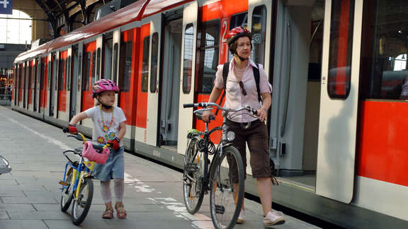 Frau und Mädchen schieben ihre Fahrräder am Bahnsteig neben Zug mit geöffneten Türen
