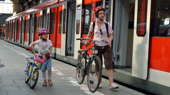 Woman and a young girl with bikes on the platform next to a red train with opened doors