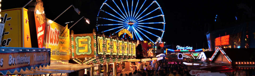 Straße mit Buden und vielen Besuchern auf dem Prämienmarkt mit Riesenrad bei Nacht