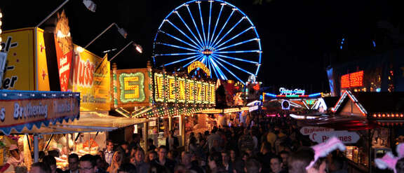 Straße mit Buden und vielen Besuchern auf dem Prämienmarkt mit Riesenrad bei Nacht