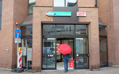 Eine Frau mit rotem MTV-Regenschirm betritt das Gebäude der Geschäftsstelle und Mobilitätszentrale