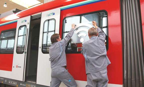 Zwei Männer kleben das WLAN-Symbol auf ein Fenster einer S-Bahn