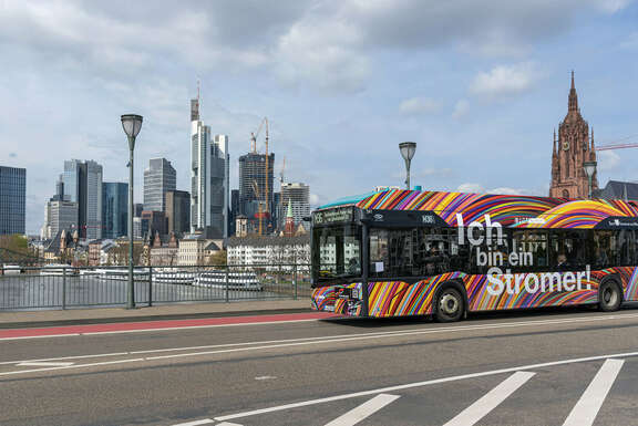 Bunt lackierter ÖPNV-Bus auf Mainbrücke vor der Frankfurter Skyline