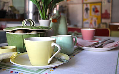Tischgedeck mit gelber Kaffeetasse, grünem Milchkännchen und rosa Kaffeetasse