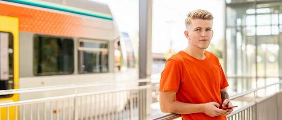 Schüler mit Smartphone in der Hand vor einem zug