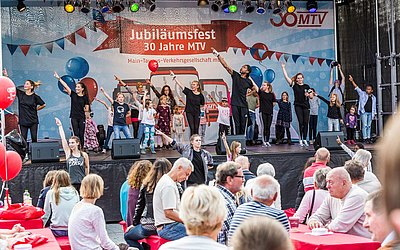 Kinder und Jugendliche performen Streetdance auf der Jubiläumsbühne. Davor sind Tische mit Zuschauern. 