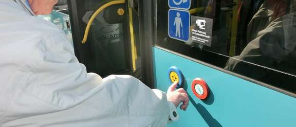 Mobilitätstraining im Bus Alter Mann betätigt Tür-Taste an der Außenseite eines Linienbusses