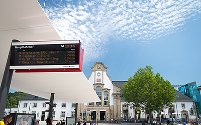digitale Anzeigetafel am Bahnhofs-Vorplatz, im Hintergrund das Bahnhofs-Gebäude