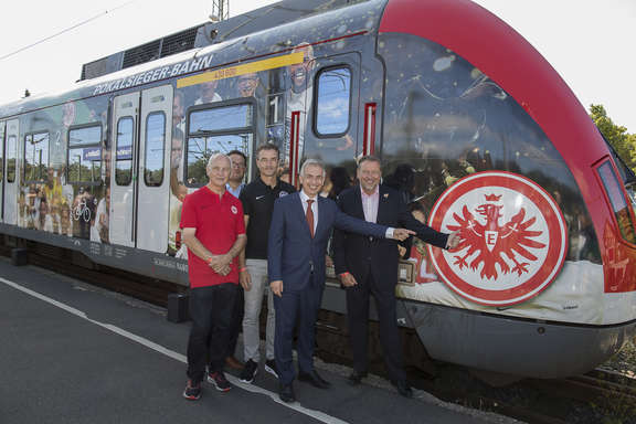 Pokalsieger-S-Bahn Personengruppe zeigt auf Logo der Eintracht auf der S-Bahn