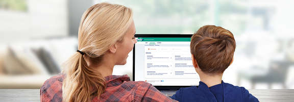 A woman and a boy are sitting in front of a computer showing the RMV-Ticketshop