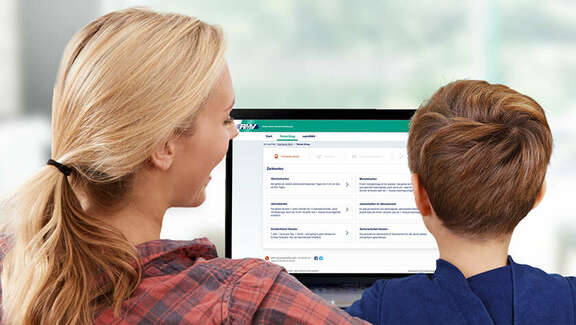 A woman and a boy are sitting in front of a computer showing the RMV-Ticketshop