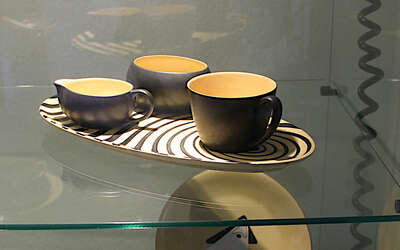 schwarz-gelbes Teetasse mit gleichfarbigen Milchkännchen und Zuckerdose auf passenden Tablett in einer Vitrine