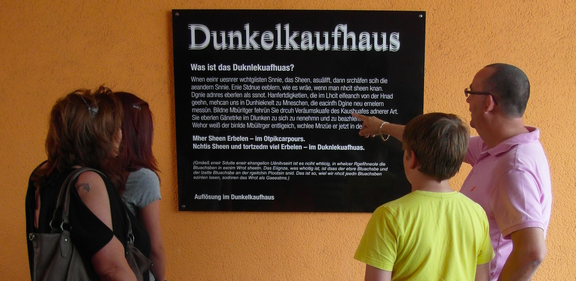 Vier Personen stehen vor einem Schild mit der Aufschrift "Dunkelkaufhaus".