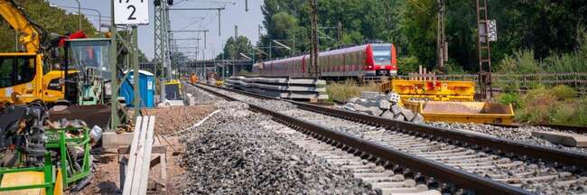 Neues Bahngleis, links Baustellenfahrzeuge, rechts S-Bahn auf bestehendem Gleis