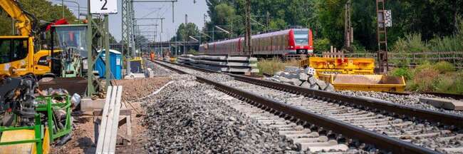 Neues Bahngleis, links Baustellenfahrzeuge, rechts S-Bahn auf bestehendem Gleis