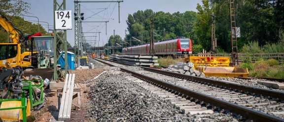 Neues Bahngleis, links Baustellenfahrzeuge, rechts S-Bahn auf bestehendem Gleis