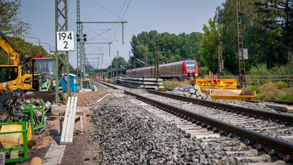 Neues Bahngleis, links Baustellenfahrzeuge, rechts S-Bahn auf bestehendem Gleis