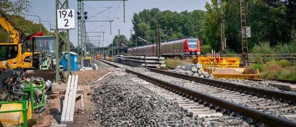 Neues Bahngleis, links Baustellenfahrzeuge, rechts S-Bahn auf bestehendem Gleis