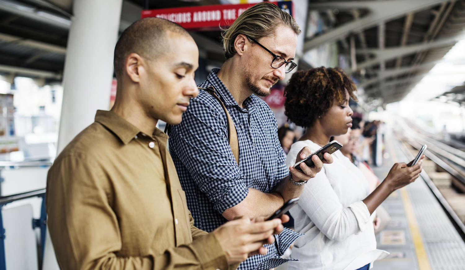 Personen mit Smartphone am Bahnhof