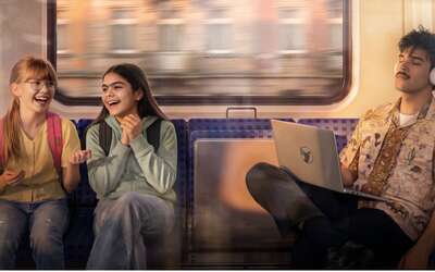 Zwei Jugendliche sitzen in einer Bahn, daneben ein junger Mann mit Kopfhörern und Laptop