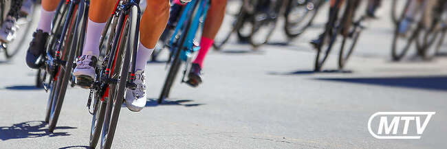 Gruppe von Rennradfahrern in einem Straßenradrennen, dicht hintereinander fahrend, mit Fokus auf Beine, Fahrräder und Geschwindigkeit auf der Strecke.