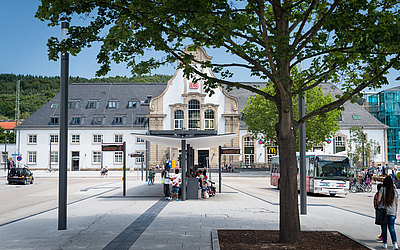 weitläufiger Bahnhofsvorplatz, mittig Bushaltestelle, im Hintergrund Bahnhofsgebäude