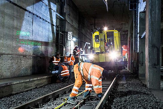Arbeiter und Bauzug im Tunnel Arbeiter verlegt Kabel an den Gleisen und im Hintergrund sind weitere Arbeiter und ein Bauzug