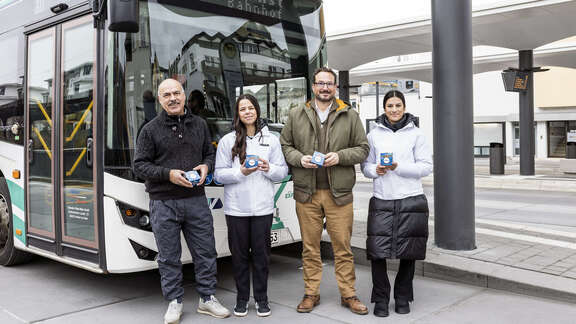 2 Männer und zwei Frauen stehen vor einem Linienbus am Busbahnhof Bad Soden und halten abgepackten Kuchen in der Hand.