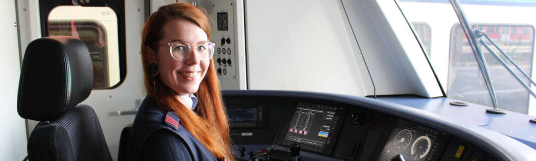 Frau in der Führerkabine einer S-Bahn mit Monitoren und Fahrplanheft