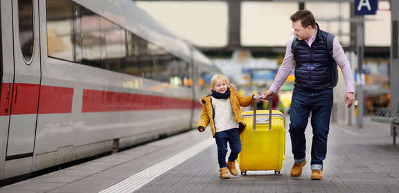 Vater und Sohn ziehen einen Reisekoffer am Bahngleis neben einem Zug