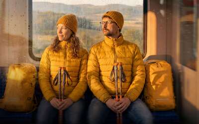 Ein Paar sitzt mit gepackten Rucksäcken in einer Bahn