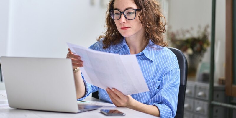 Frau vor Laptop schaut auf Unterlagen