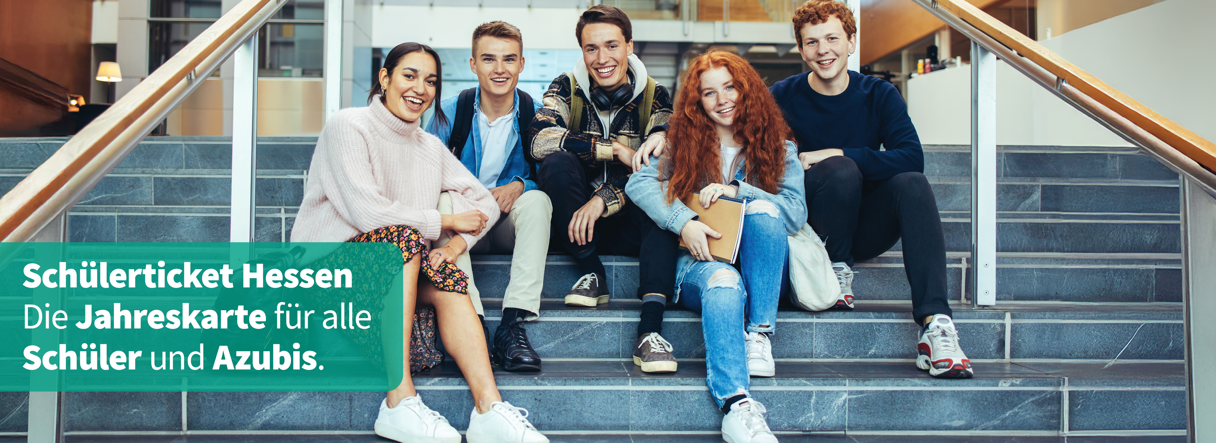Zwei Schülerinnen und drei Schüler sitzen in einer Schule auf einer Treppe