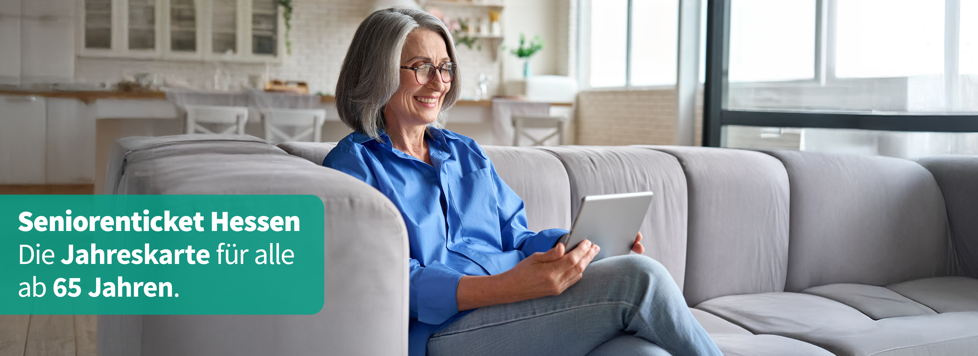 Seniorin in Wohnzimmer schaut lächelnd auf Tablet.