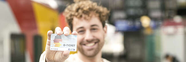 D-Ticket Lachender Mann hält Deutschland-Ticket in die Kamera